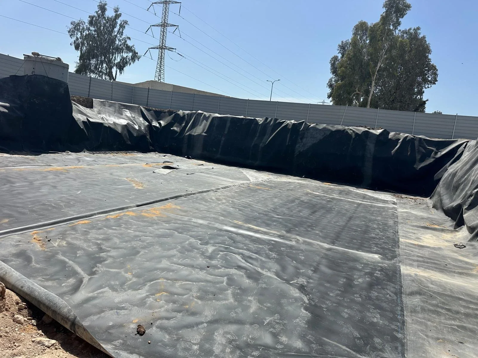 קרקעית בור מכוסה יריעת איטום שחורה עם תפרי ריתוך גלויים, דפנות מכוסות יריעה