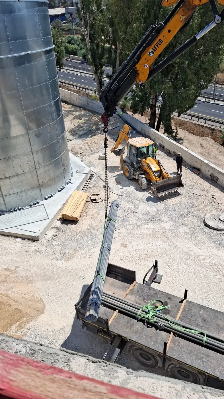 מנוף פורק צרור צינורות ממשאית באתר, מחפרון ברקע