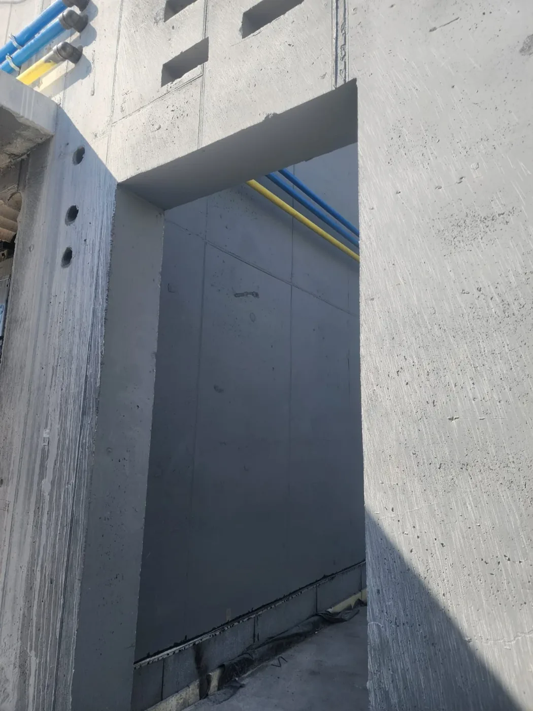 פתח דלת בקיר בטון ומבעדו נראית צנרת כחולה וצהובה על הקיר הפנימי