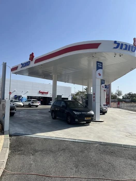 תחנת סונול חדשה ופעילה: סככת תדלוק לבנה עם פס אדום, עמדות תדלוק ורכבים, ומבנה החנות ברקע