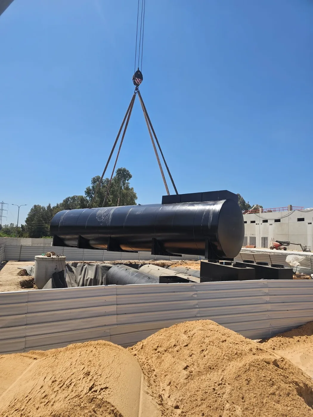 מיכל דלק גלילי תלוי על רצועות מנוף מעל גדר אתר בנייה
