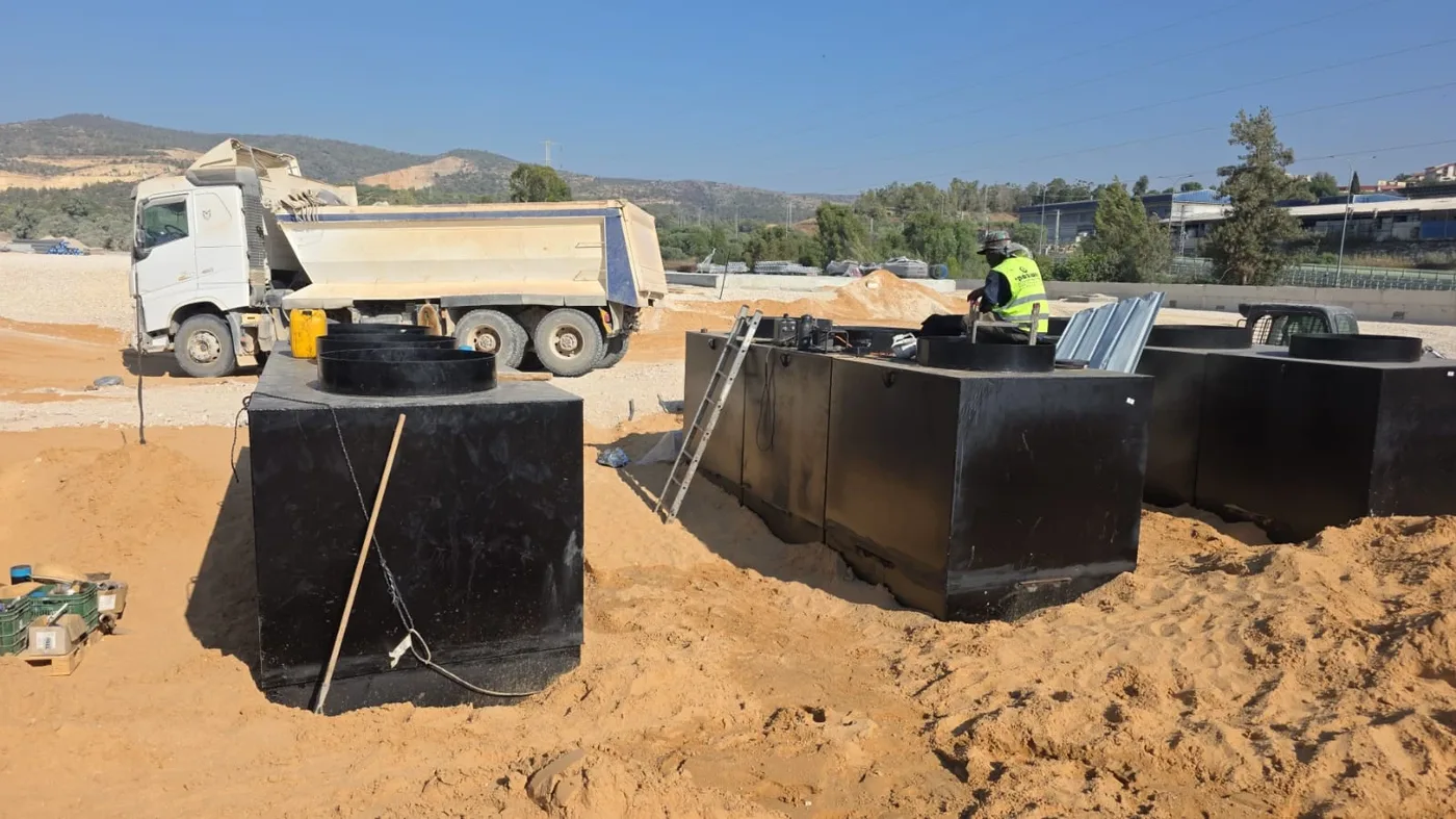 מיכלי דלק שחורים עם שוחות עליונות על מצע חול, לצד משאית
