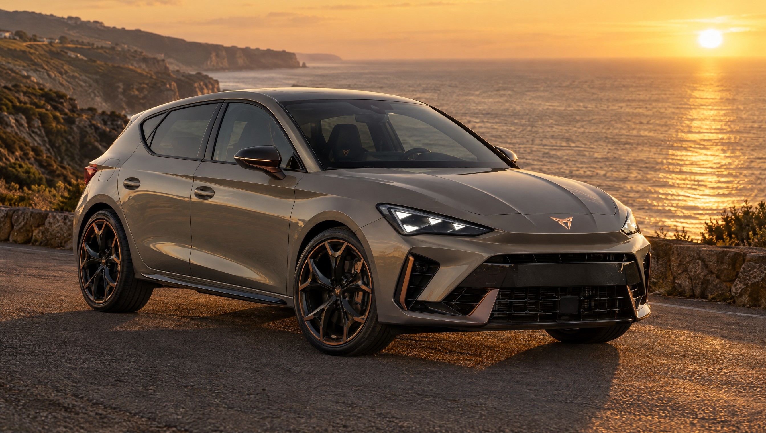 The grey-beige CUPRA Leon on a cliff road above the sea at sunset